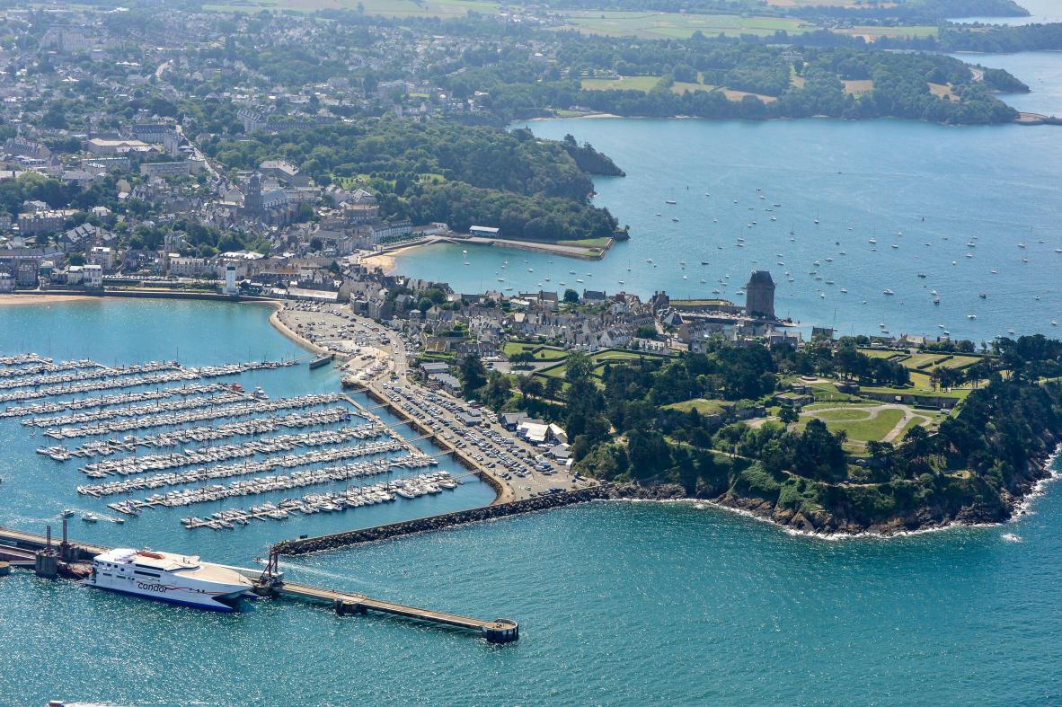 Vue aérienne du port des Bas Sablons à Saint-Malo avec bateaux alignés, la Cité d’Aleth arborée et un ferry blanc à quai.