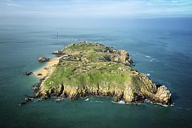 Vue aérienne de l’île de Cézembre montrant ses plages de sable, sa végétation verte et les côtes rocheuses de Saint-Malo.