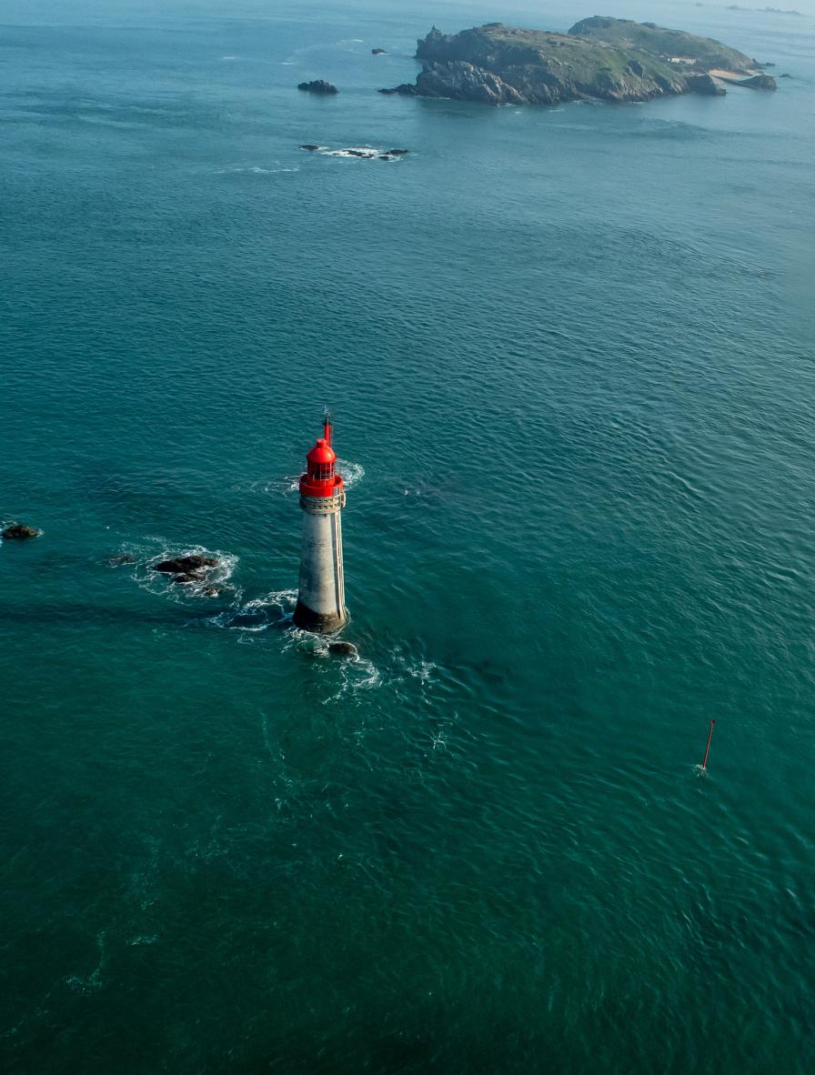 Phare blanc à dôme rouge isolé en pleine mer turquoise. Vue plongeante sur les courants marins près des côtes de Saint-Malo.