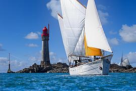 Voilier traditionnel blanc sous voiles naviguant devant le phare du Grand Jardin par temps ensoleillé à Saint-Malo.