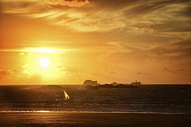 Windsurfeur naviguant sur mer agitée sous un ciel doré intense au couchant avec silhouettes de forts malouins.