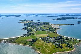 Panorama aérien de l’île d’Arz révélant ses champs verts, son littoral sablonneux et les eaux bleues du Golfe du Morbihan.