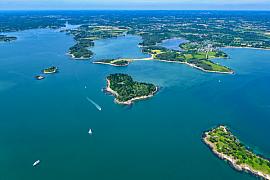 Vue aérienne des îles Er Runio et Sept Îles dans le Golfe du Morbihan avec eaux bleues et végétation verdoyante.