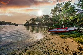 Voilier Caravelle rouge sur le sable bordé de pins au coucher du soleil, Pointe du Blaire dans le Golfe du Morbihan.