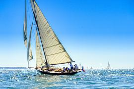 Voilier classique Pen Duick naviguant sous voiles blanches sur mer bleue scintillante sous un franc soleil breton.