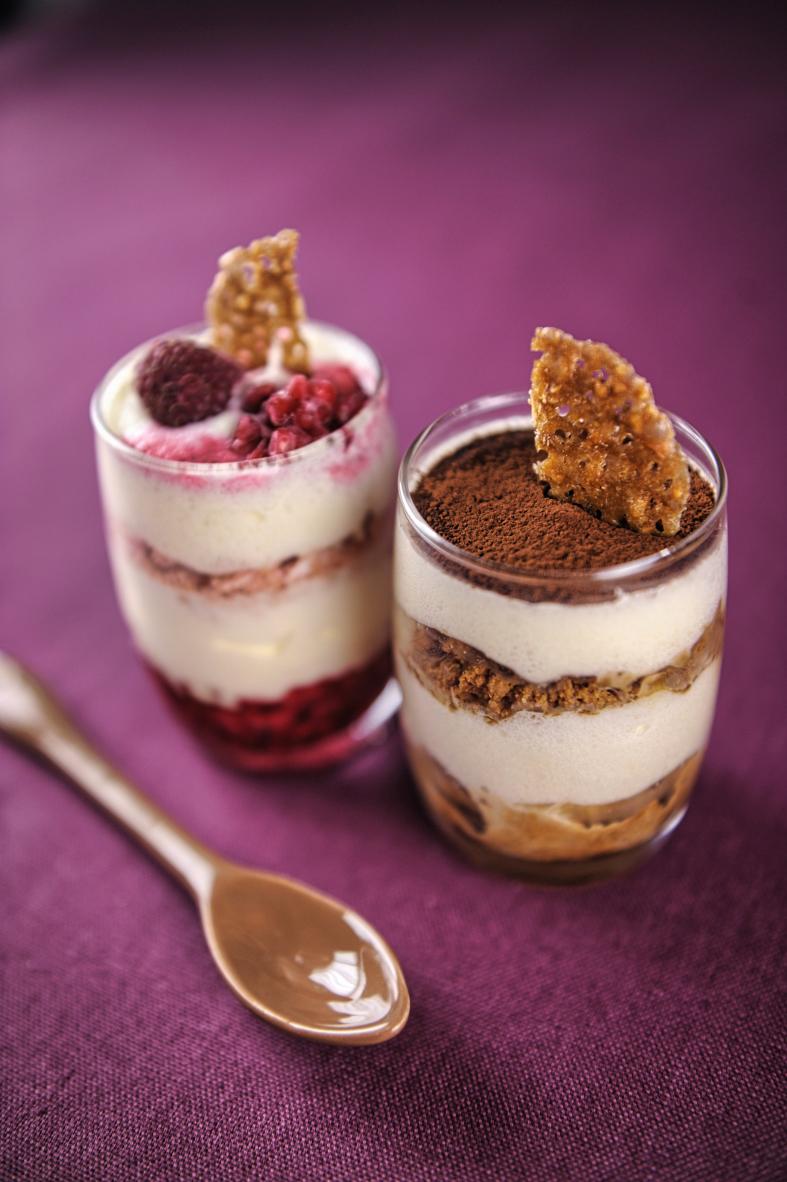 Deux verrines de tiramisu, l’une aux fruits rouges et l’autre au cacao, sur un fond violet tamisé.