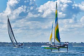 Catamaran Flying Phantom volant sur foils en baie de Saint-Malo sous un ciel nuageux et ensoleillé en pleine mer.