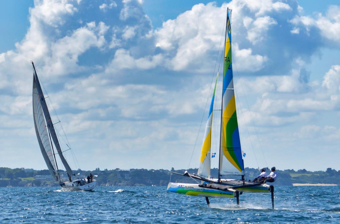 Catamaran Flying Phantom volant sur foils en baie de Saint-Malo sous un ciel nuageux et ensoleillé en pleine mer.