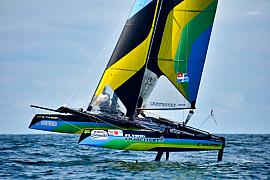 Catamaran Flying Phantom aux voiles jaune et vert volant sur foils en baie de Saint-Malo par mer calme.