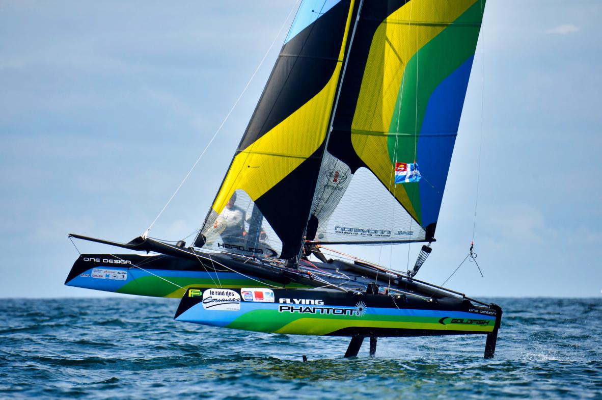 Catamaran Flying Phantom aux voiles jaune et vert volant sur foils en baie de Saint-Malo par mer calme.