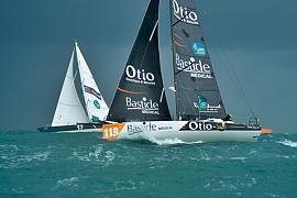 Deux voiliers de course fendant les vagues lors du départ de la Route du Rhum sous un ciel chargé à Saint-Malo.