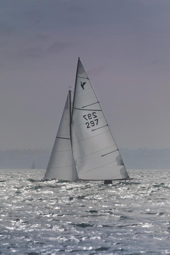 Voilier Cormoran aux voiles blanches avec numéro 297 naviguant sur une mer agitée sous un ciel gris en Bretagne.