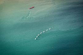 Voiliers blancs alignés sur mer turquoise avec un canot de sécurité rouge, vue verticale, lumière naturelle.