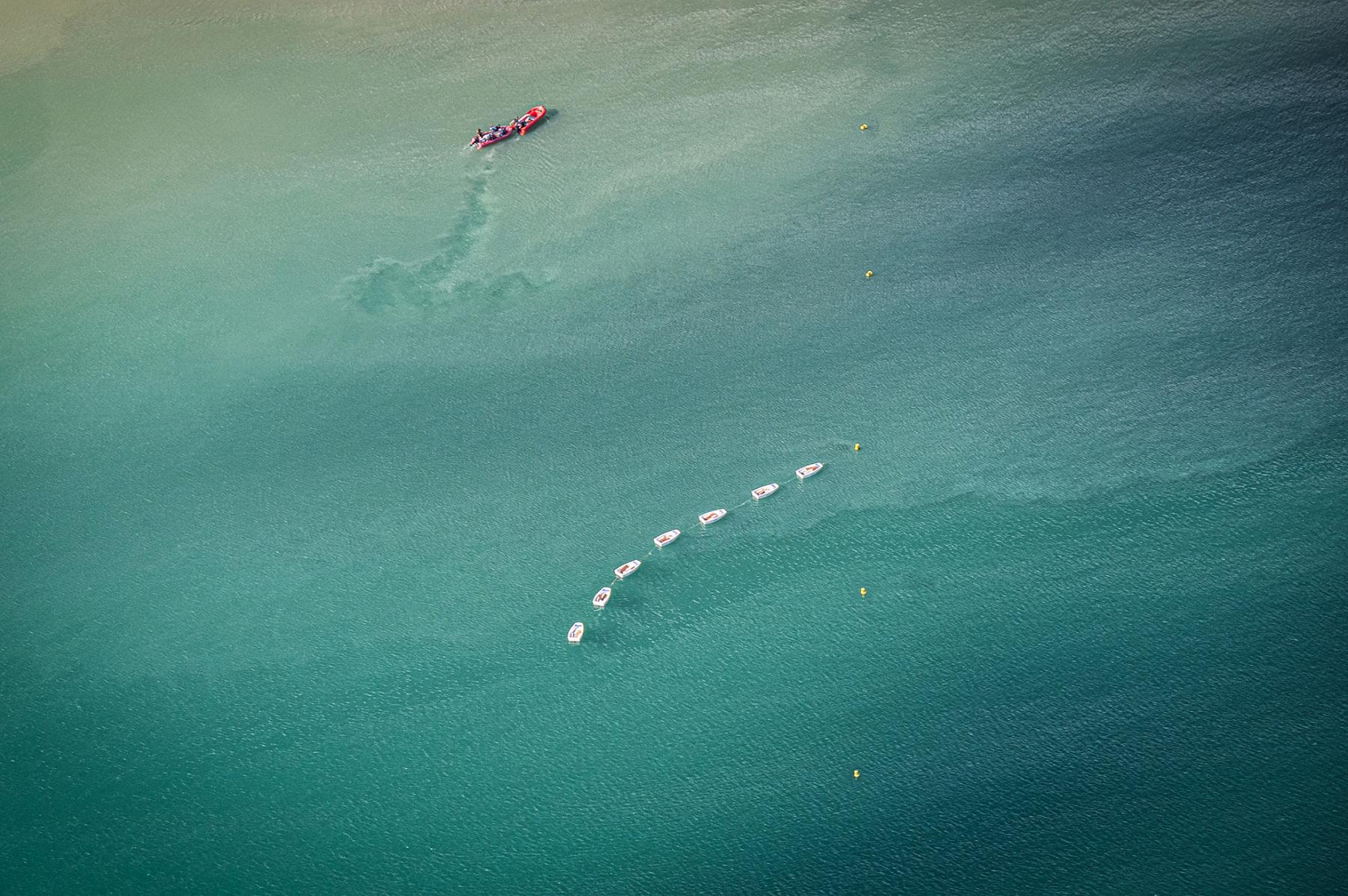 Voiliers blancs alignés sur mer turquoise avec un canot de sécurité rouge, vue verticale, lumière naturelle.