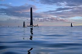 Plusieurs trimarans sur une mer calme aux reflets bleus sous un ciel nuageux de fin de journée en Bretagne.