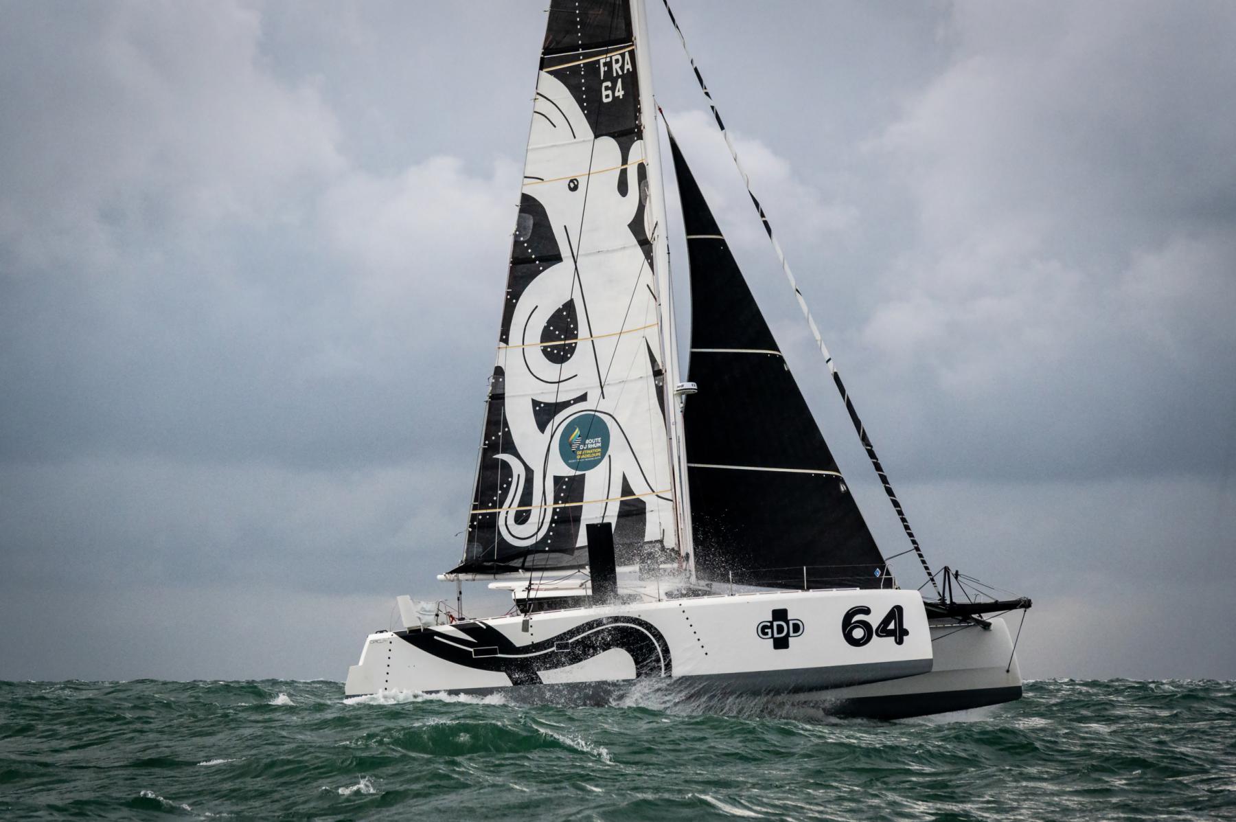 Catamaran GDD blanc et noir sur mer agitée, voiles avec motif poulpe, navigation sportive sous ciel gris.