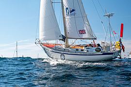 Voilier de course blanc aux voiles déployées sur une mer agitée sous un ciel bleu lors du départ d’une régate.