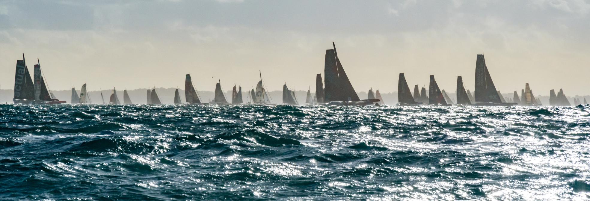 Voiliers de course sur mer agitée à Saint-Malo pour le départ de la Route du Rhum sous un ciel voilé.