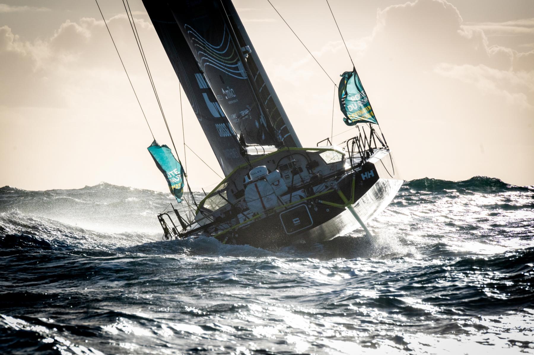 Voilier Class 40 Crosscall gîtant sur une mer agitée face au soleil lors du départ de la Route du Rhum à Saint-Malo.