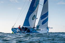 Voilier Class 40 bleu et blanc naviguant sur une mer agitée sous un ciel clair à Saint-Malo lors de la Route du Rhum