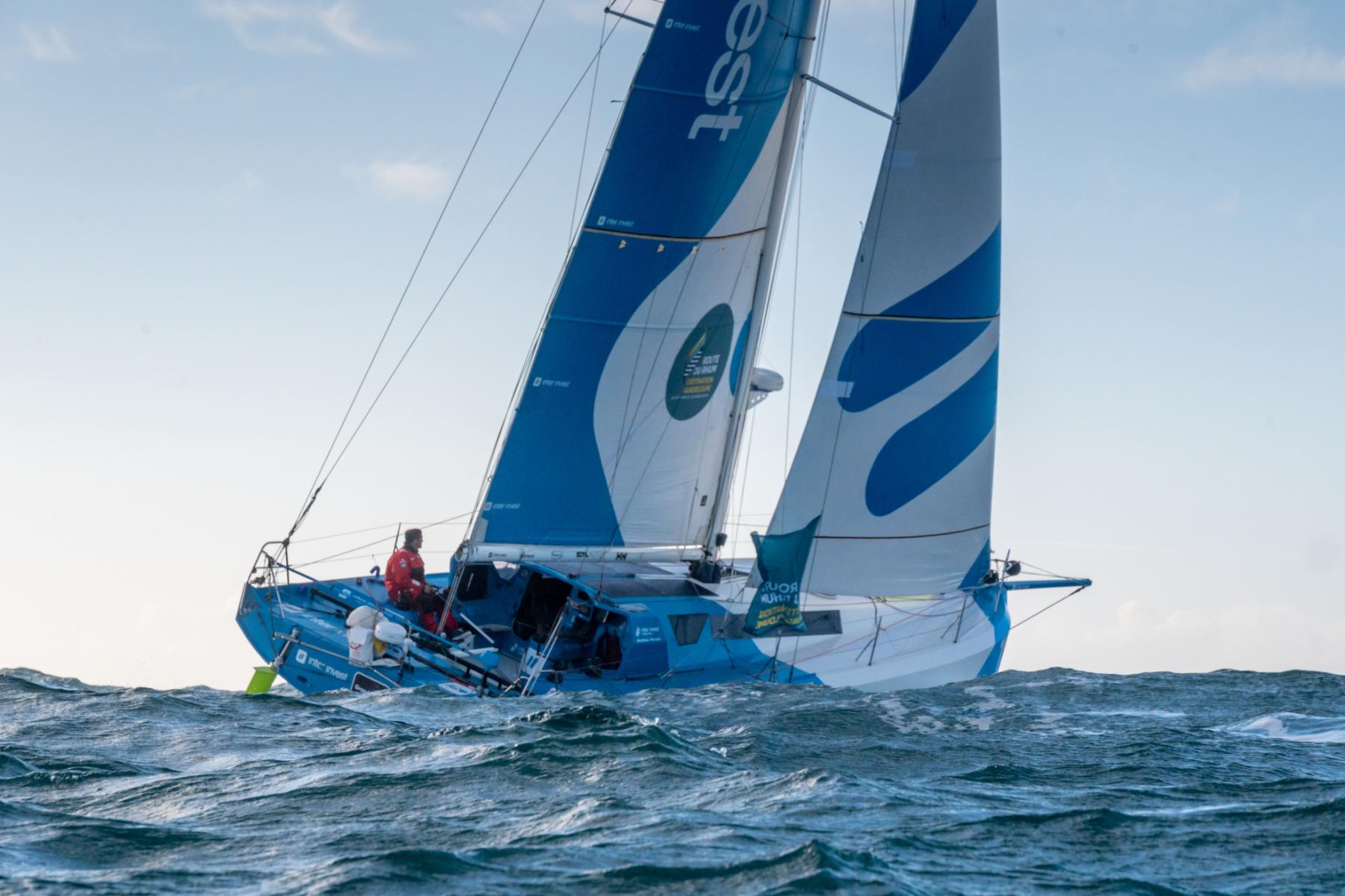 Voilier Class 40 bleu et blanc naviguant sur une mer agitée sous un ciel clair à Saint-Malo lors de la Route du Rhum