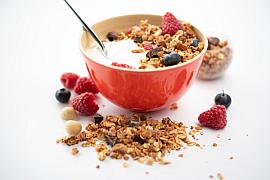 Bol rouge de granola croustillant au fromage blanc de brebis avec framboises et myrtilles sur fond blanc lumineux