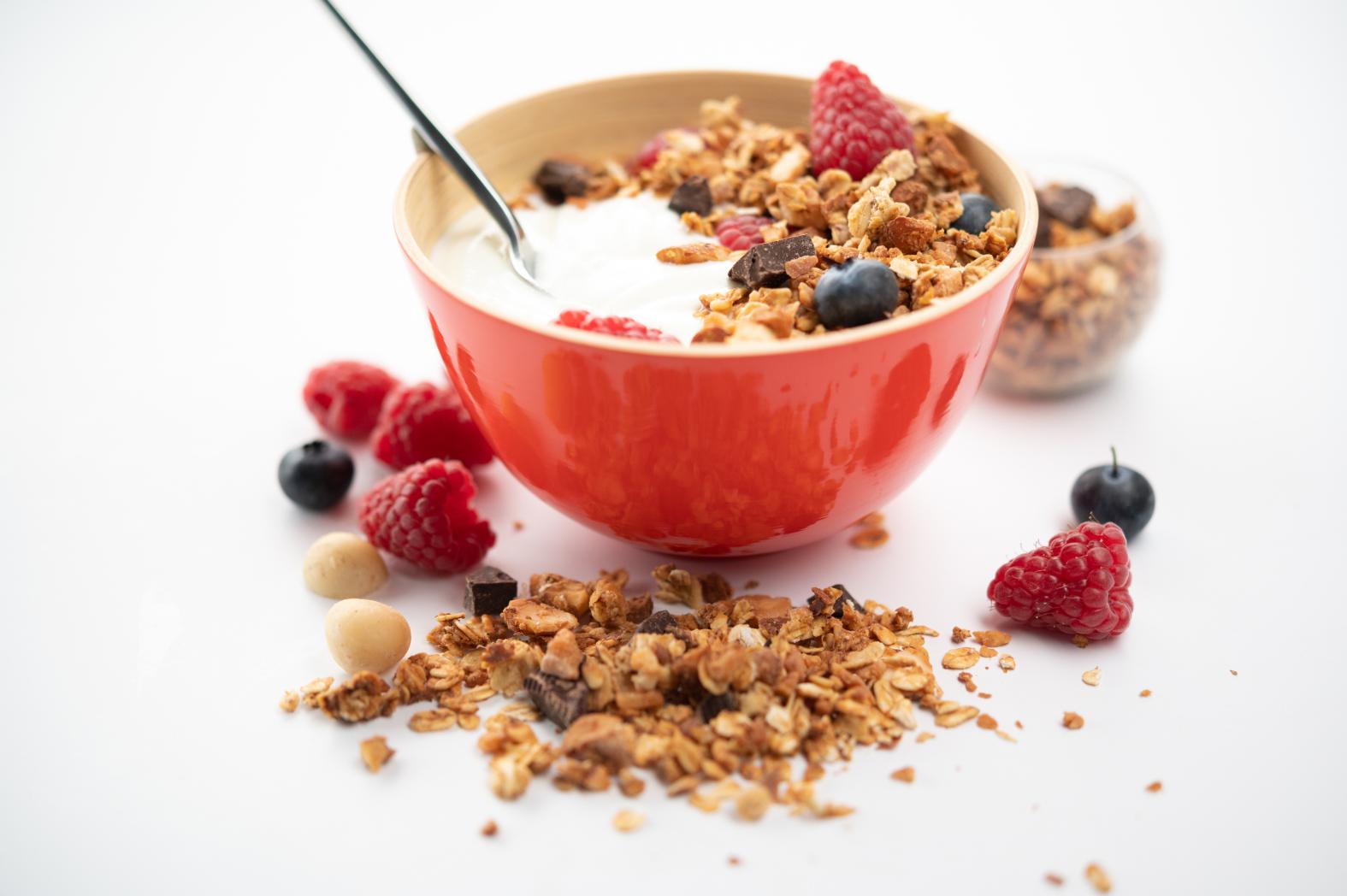 Bol rouge de granola croustillant au fromage blanc de brebis avec framboises et myrtilles sur fond blanc lumineux