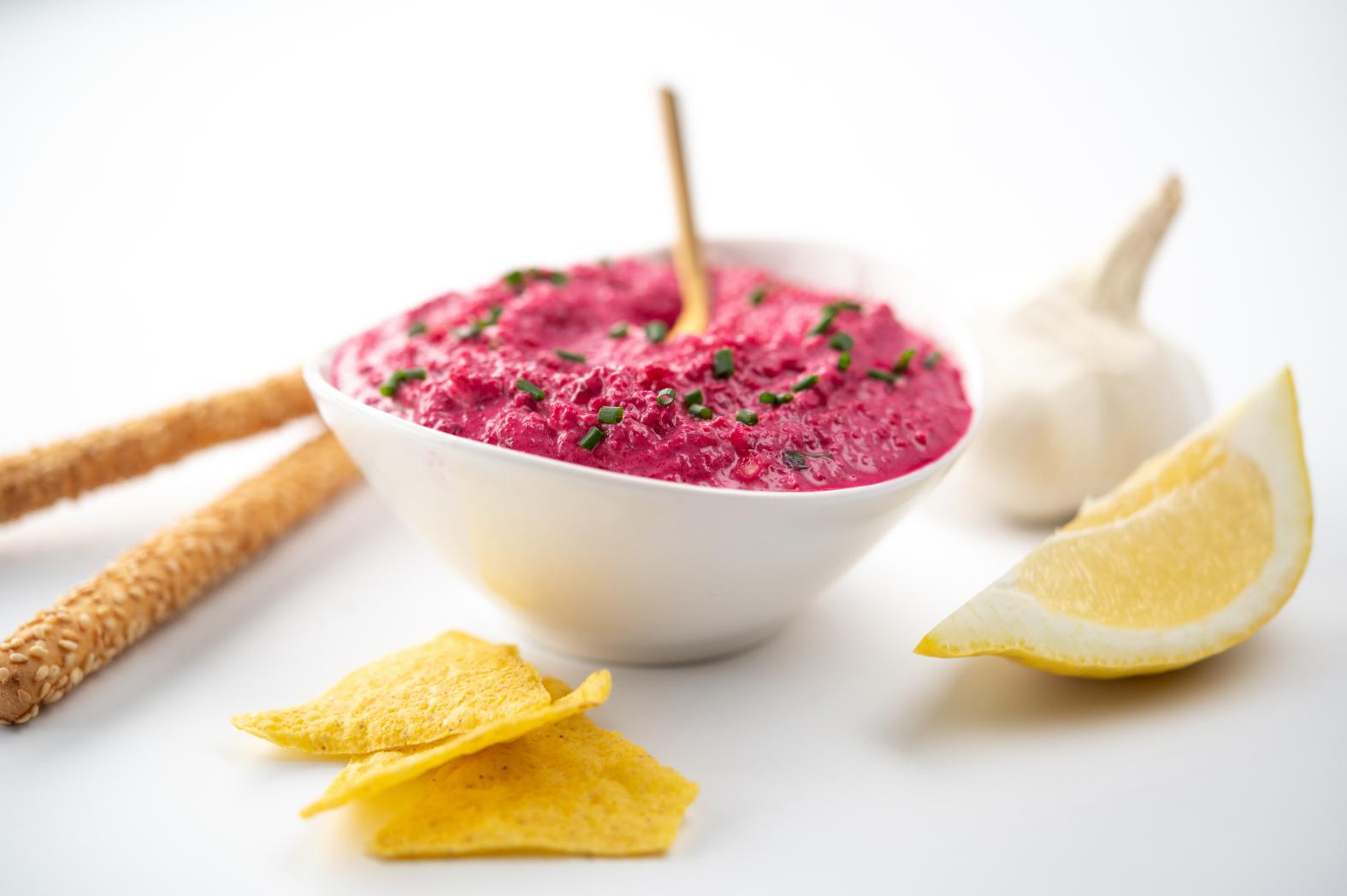Crème de betterave rose dans un bol blanc avec chips de maïs et citron sur fond blanc, lumière douce.