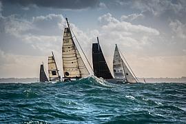 Voiliers monocoques sur mer agitée à Saint-Malo, voiles tendues sous un ciel chargé et lumineux.