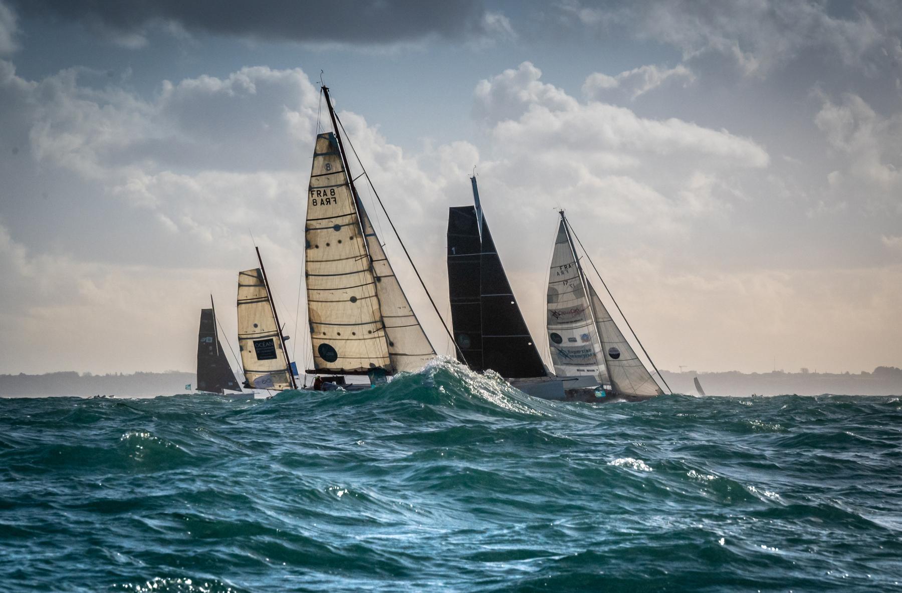 Voiliers monocoques sur mer agitée à Saint-Malo, voiles tendues sous un ciel chargé et lumineux.