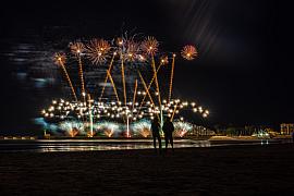Feu d’artifice doré éclatant au-dessus de l’océan avec silhouettes de spectateurs sur la plage de nuit.
