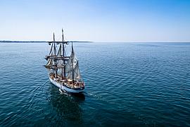 Trois-mâts barque Le Français naviguant sur mer bleue calme sous un ciel dégagé, vue plongeante ensoleillée.