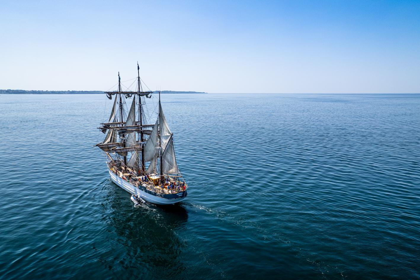 Trois-mâts barque Le Français naviguant sur mer bleue calme sous un ciel dégagé, vue plongeante ensoleillée.