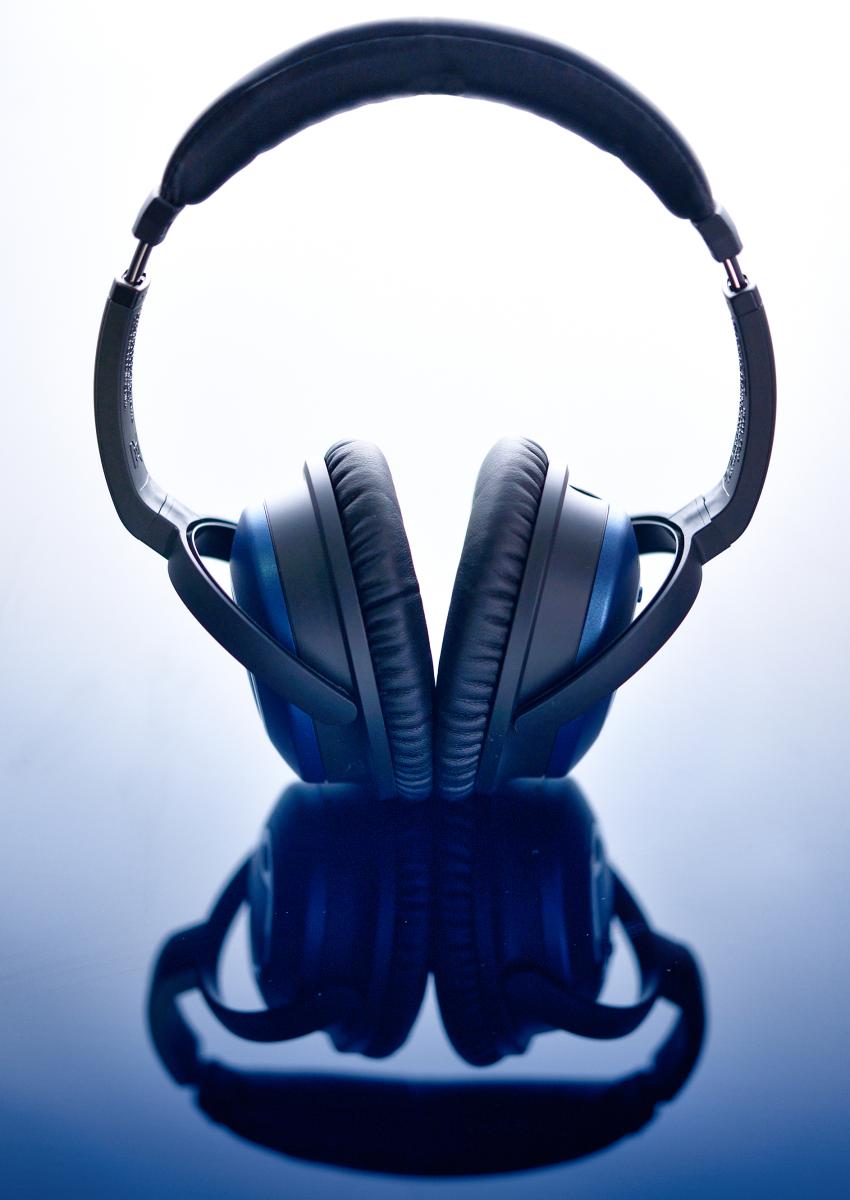 Casque audio Bose bleu reposant sur un support brillant avec reflet symétrique, éclairage studio contrasté et net.