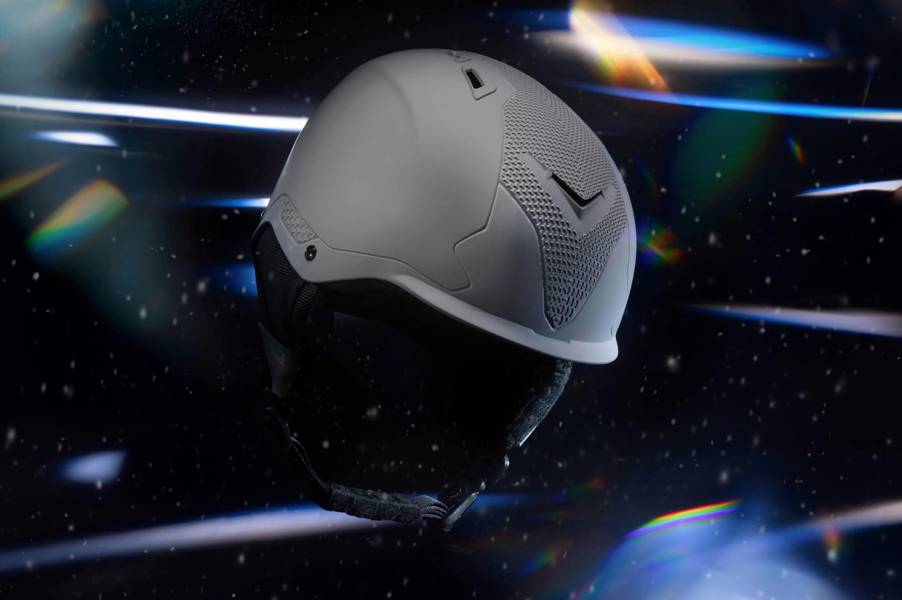 Casque de ski gris Aurak sur fond noir parsemé de neige avec effets de lumière prismatiques et reflets colorés.