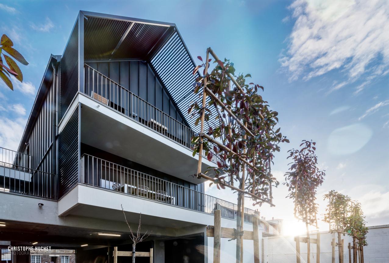 Façade contemporaine sombre et balcons blancs sous un soleil radieux avec structures en bois au premier plan.