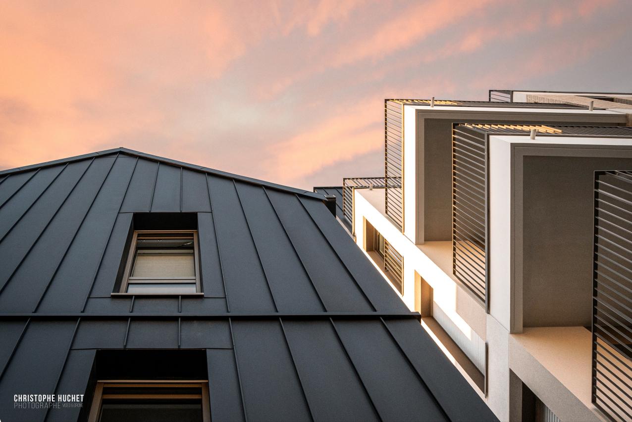 Façade en métal sombre et balcons blancs ajourés du Millésime à Rennes sous un ciel orangé de fin de journée.