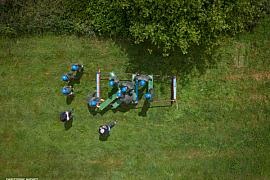 Vue drone zénitale de stagiaires en casques bleus déplaçant des madriers sur herbe lors d’un atelier leadership