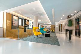 Hall d’hôtel à Cannes avec fauteuils jaune et bleu, sol blanc brillant et éclairage moderne au plafond.