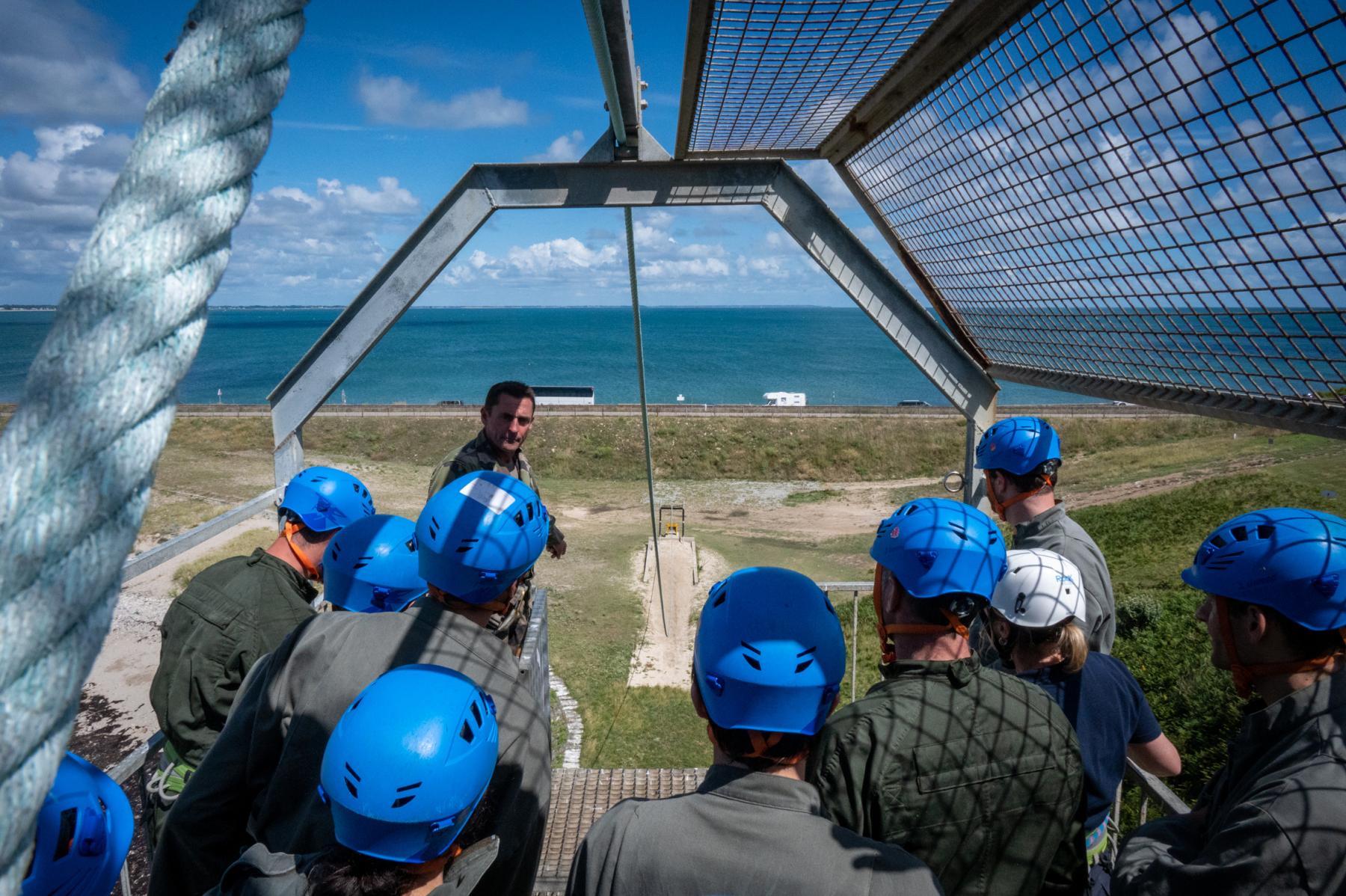 Groupe casqué sur plateforme métallique dominant la mer lors d’un exercice de leadership en Bretagne.