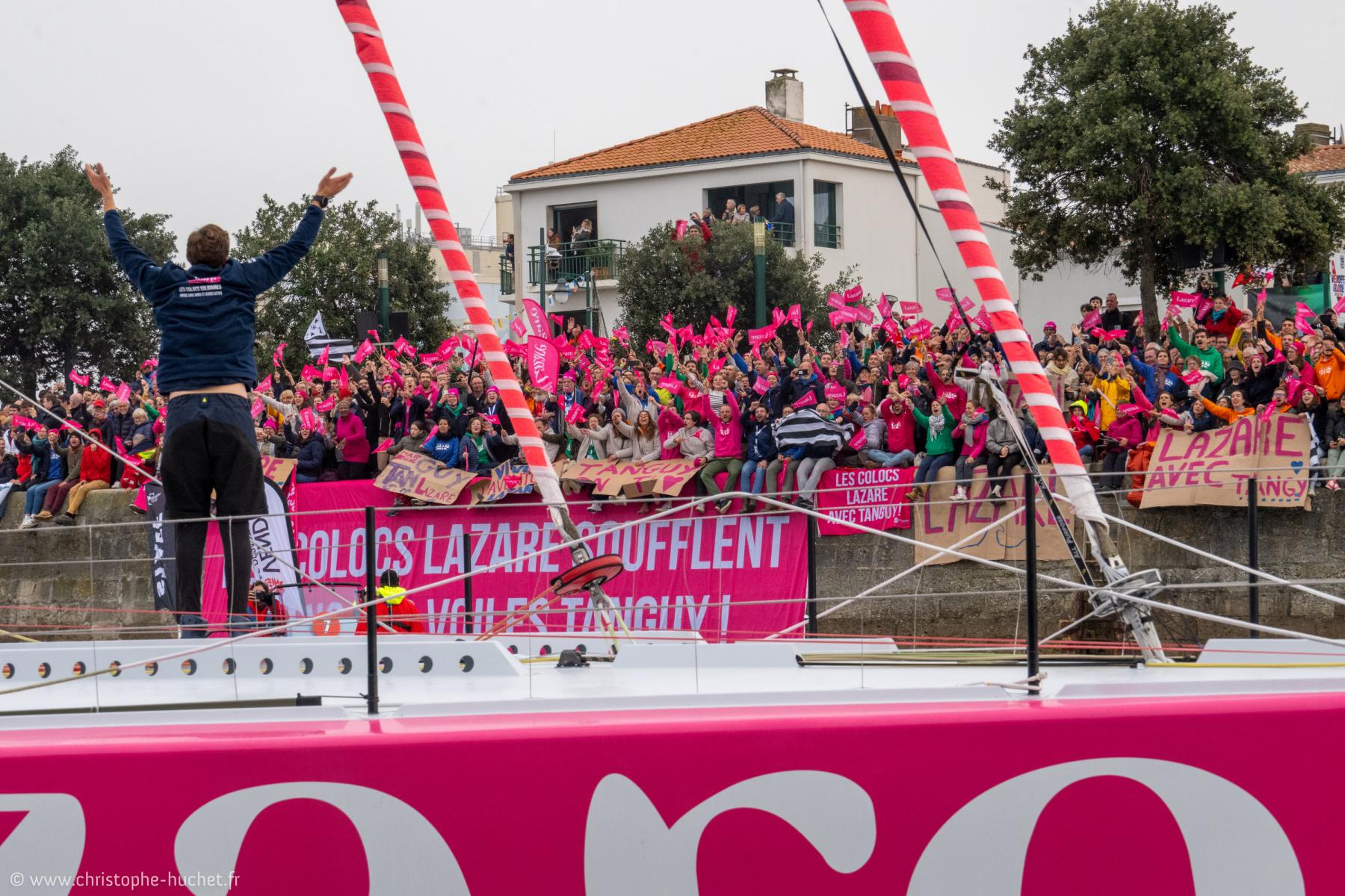Tanguy Le Turquais bras levés sur l’IMOCA Lazare devant une foule en rose aux Sables-d’Olonne.