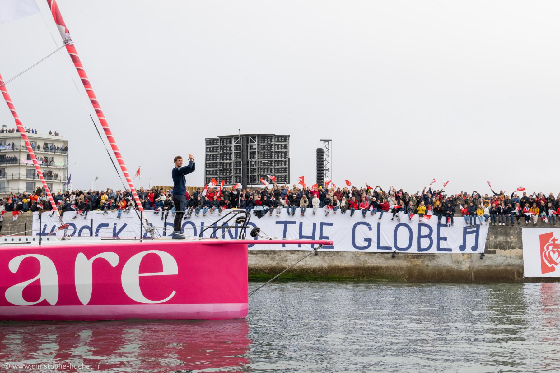 Tanguy Le Turquais debout sur l’Imoca Lazare rose devant une foule aux Sables d’Olonne lors du Vendée Globe