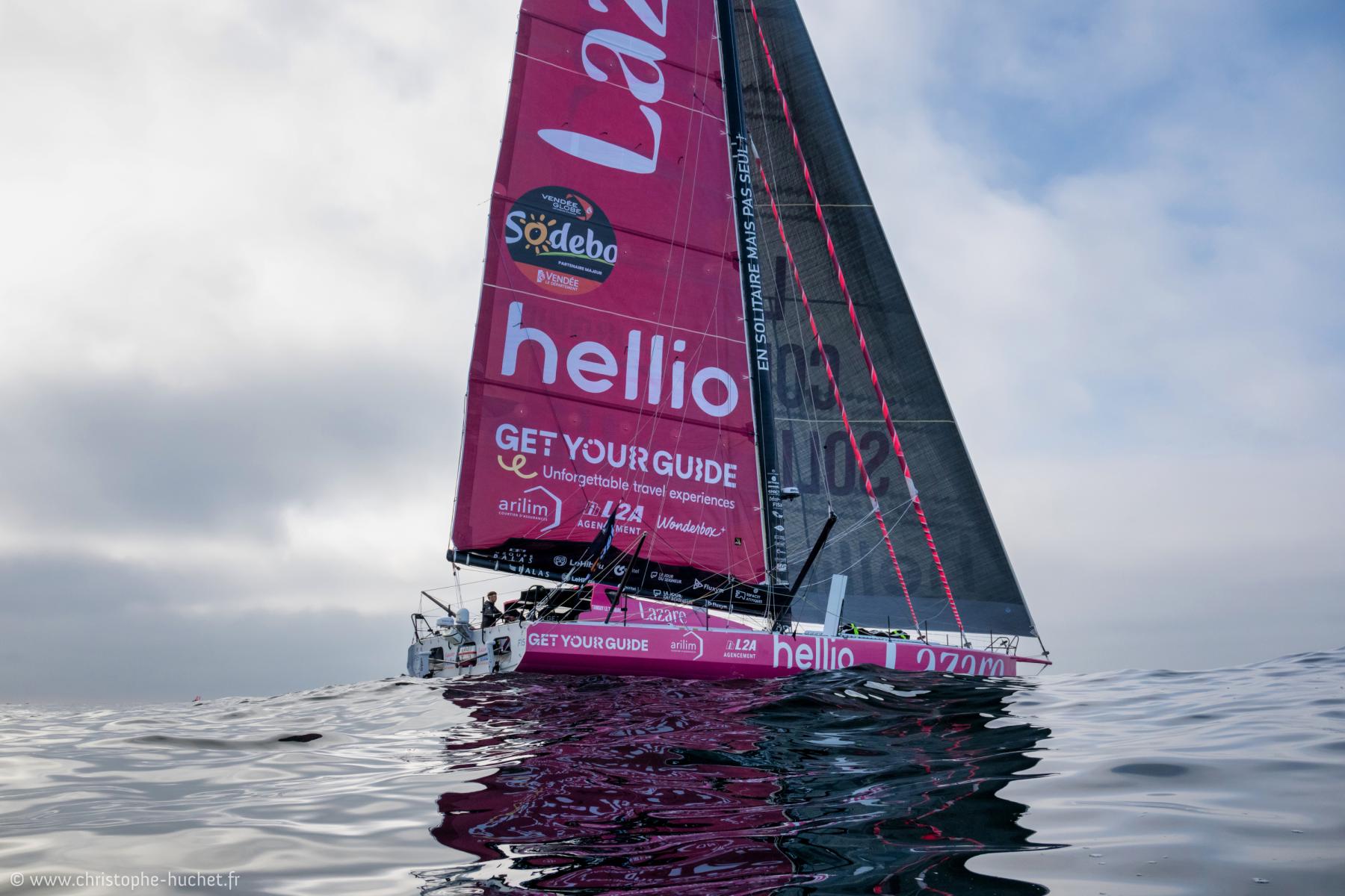 Voilier rose Imoca Lazare sur océan calme, ciel gris clair, reflets de l’eau, départ de course aux Sables-d’Olonne.