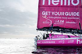 Voilier IMOCA Lazare rose sur l’eau aux Sables d’Olonne, grand voile déployée sous un ciel nuageux.