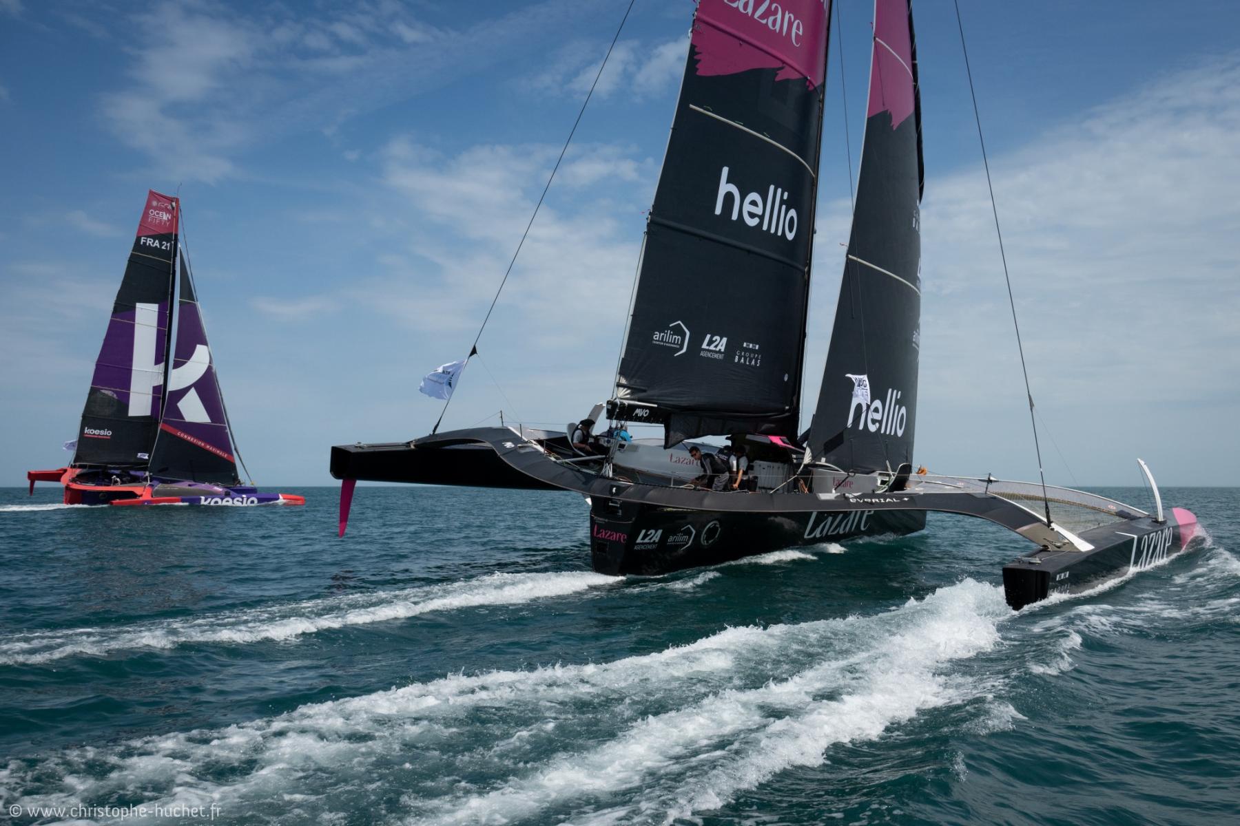 Trimaran Ocean Fifty LAZARE en course à Saint-Malo, voiles noires, sillage vif et ciel azur.