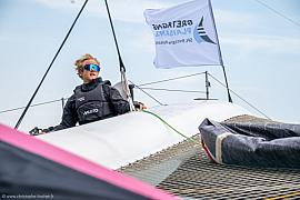 Marin sur le trimaran Ocean Fifty Lazare à Saint-Malo, portant des lunettes de soleil et une veste de quart noire.