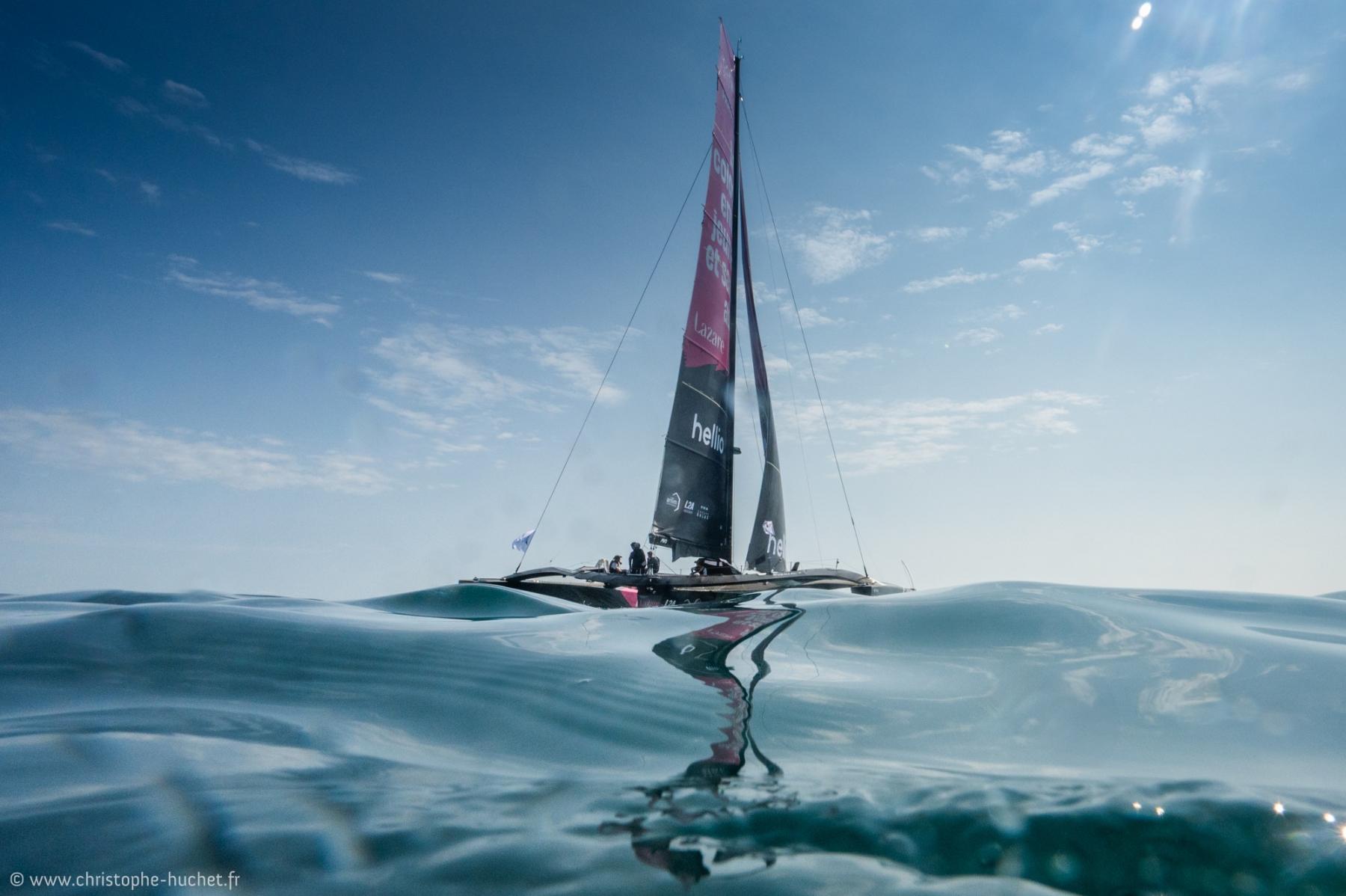 Trimaran Ocean Fifty Lazare sur mer calme à Saint-Malo avec reflets dans l’eau turquoise.