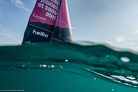 Vue au ras de l’eau d’une voile rose et noire du trimaran Lazare avec reflets marins et ciel clair à Saint-Malo