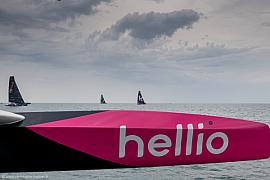 Gros plan sur la coque rose Hellio d’un trimaran Ocean Fifty naviguant à Saint-Malo par temps couvert.