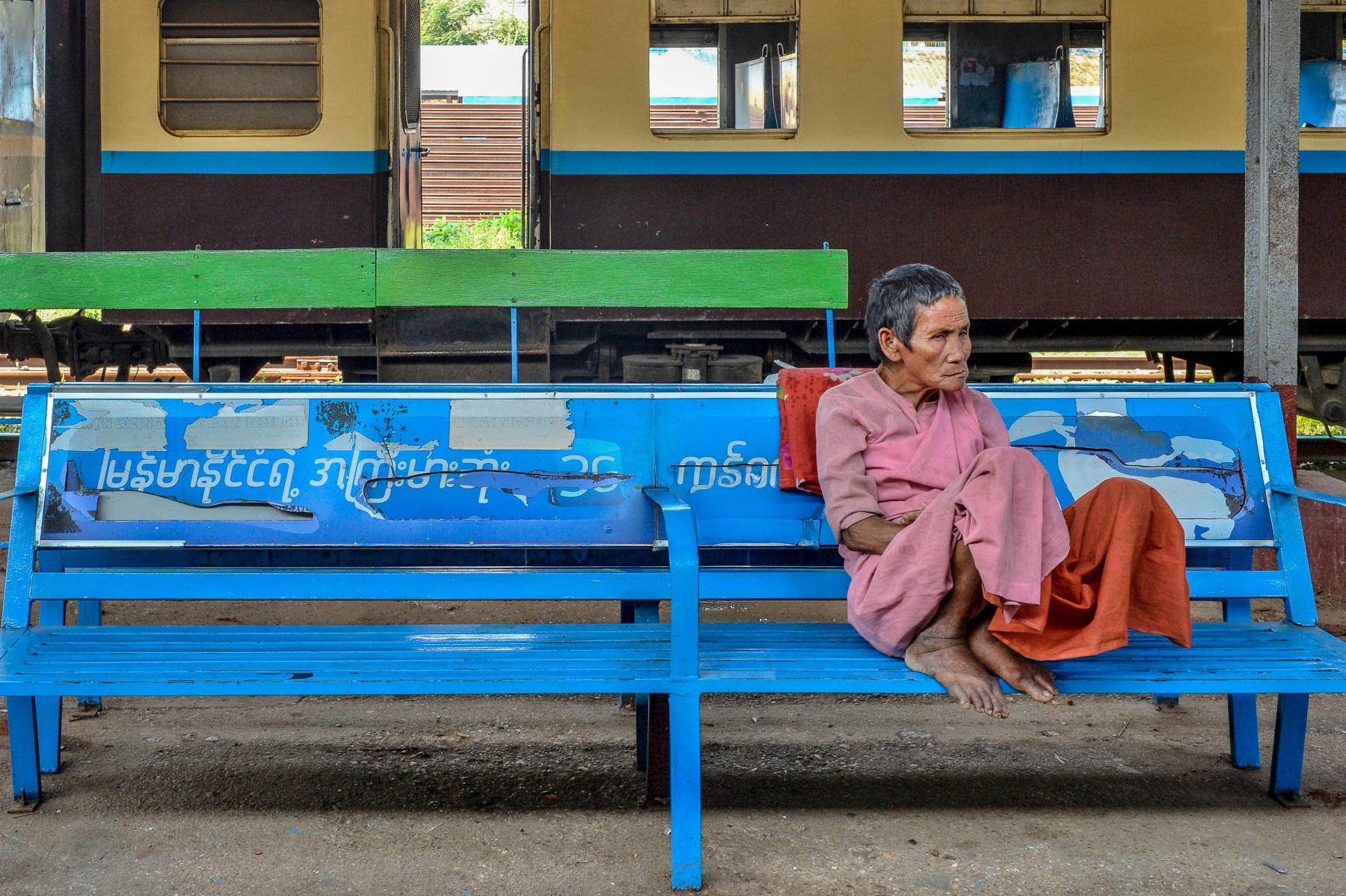 Photo Femme âgée assise sur un banc bleu dans une gare ferroviaire à Rangoon